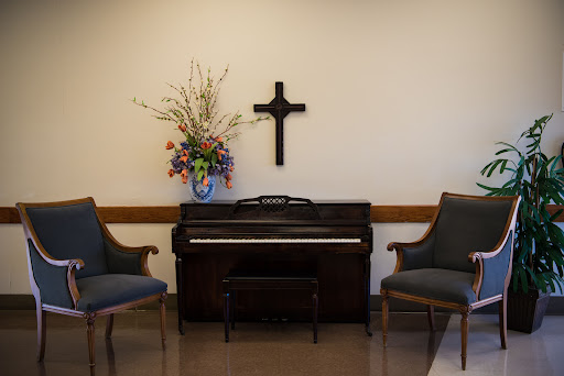 A serene corner with a piano, floral arrangement, and a cross for reflection.