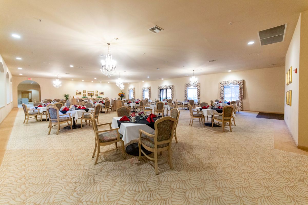 A spacious dining area with tables and chairs, softly lit by chandeliers, filled with people enjoying a meal.
