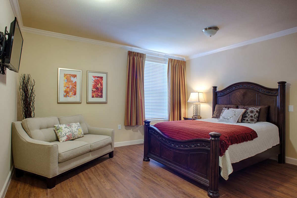 A cozy bedroom featuring a large bed with red bedding, a beige couch, and warm lighting.