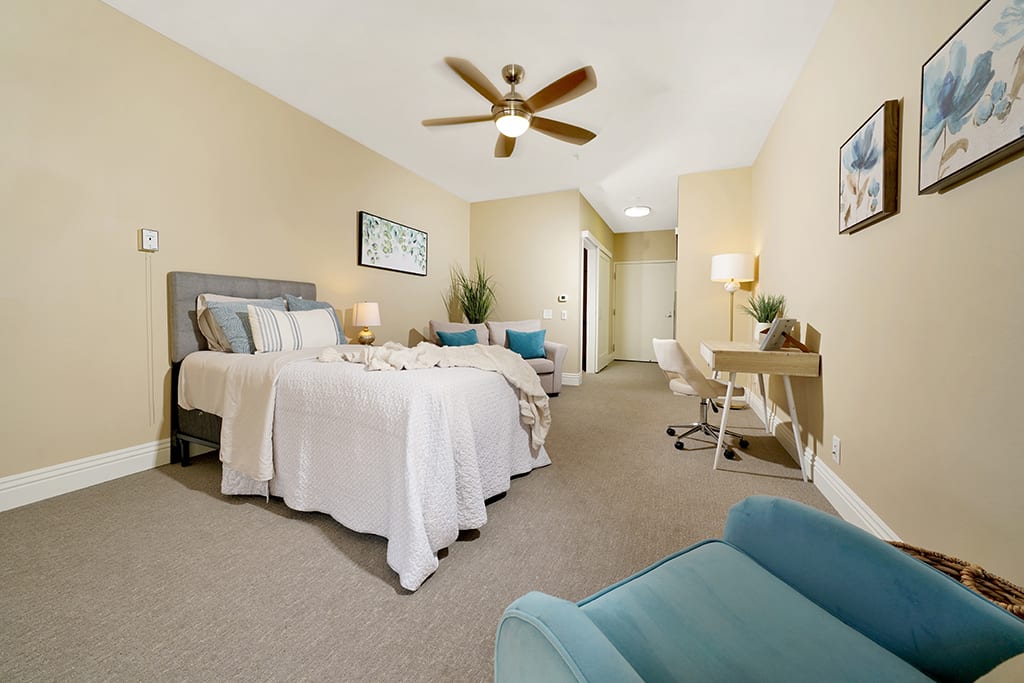 A cozy bedroom with a double bed, ceiling fan, and a work desk.