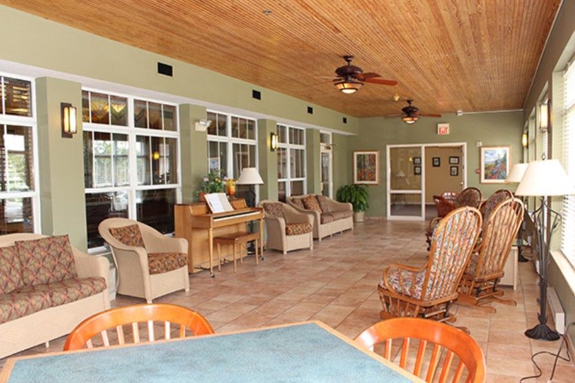 A spacious sunroom featuring comfortable seating, large windows, and a wooden ceiling with ceiling fans.