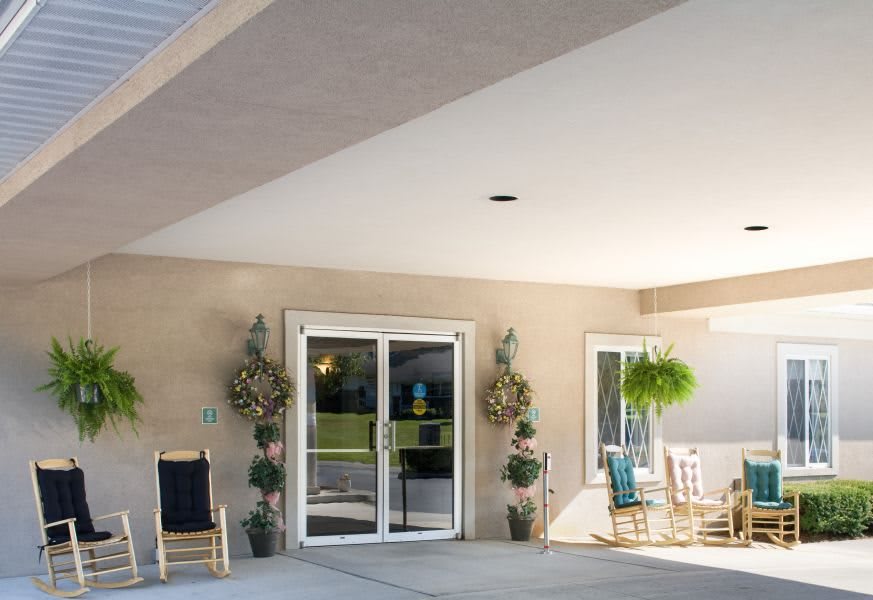 A cozy porch with chairs, potted plants, and a sliding glass door entrance.