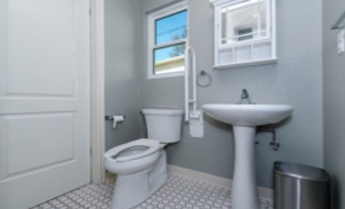 A small bathroom with a toilet, pedestal sink, and mirror under a window.