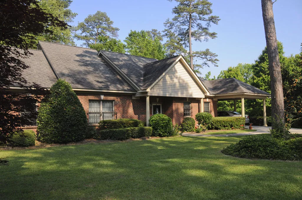 A charming brick house with a well-maintained front yard, surrounded by lush trees and bushes.