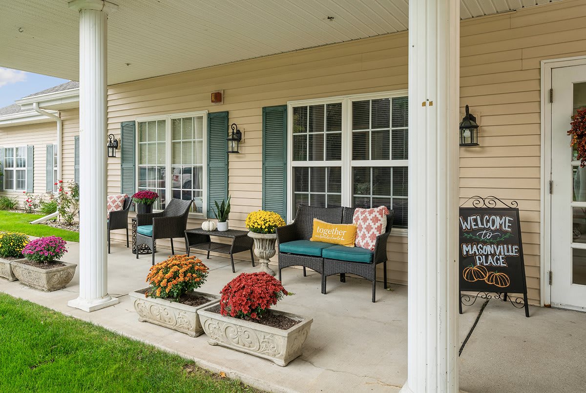 A charming porch with outdoor seating, colorful pillows, flower pots, and a welcome sign.
