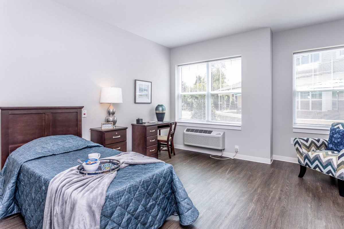A bright and cozy bedroom with a bed, desk, and large window allowing natural light.