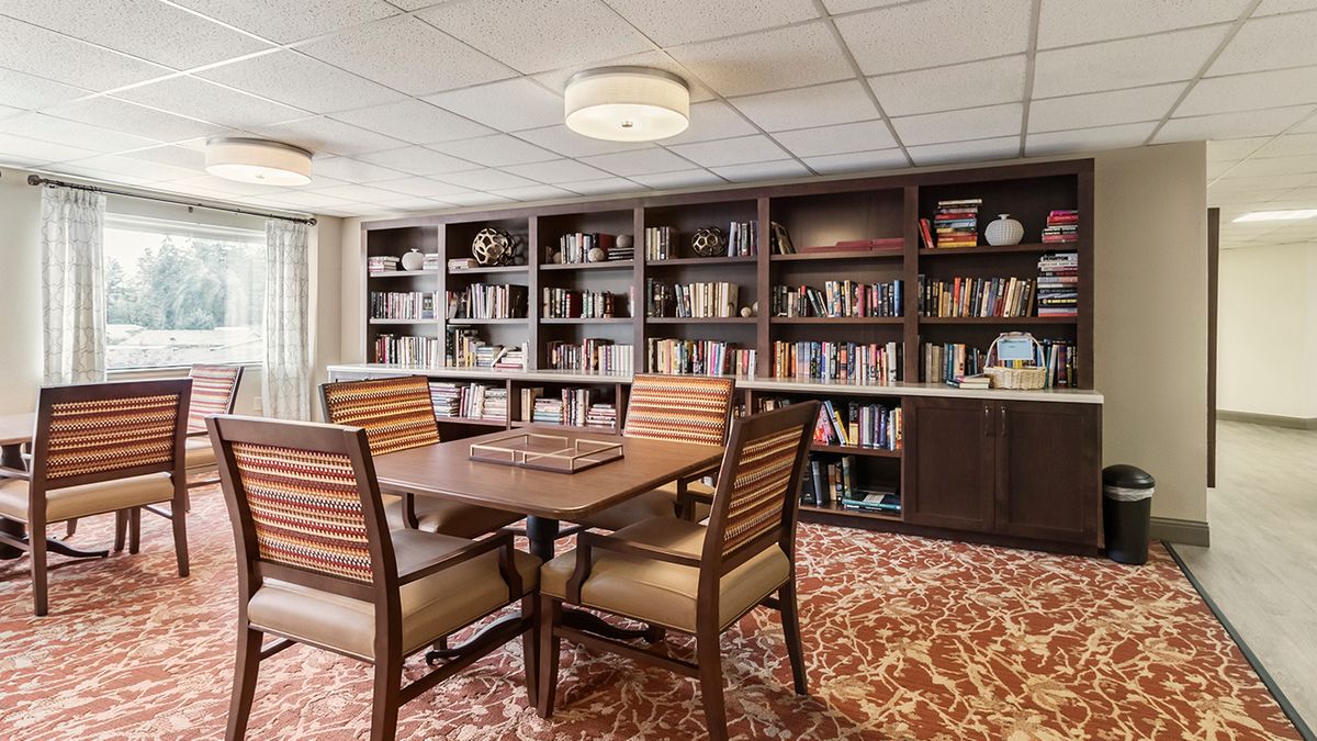 A cozy library room with a wooden table and chairs surrounded by bookshelves filled with various books.