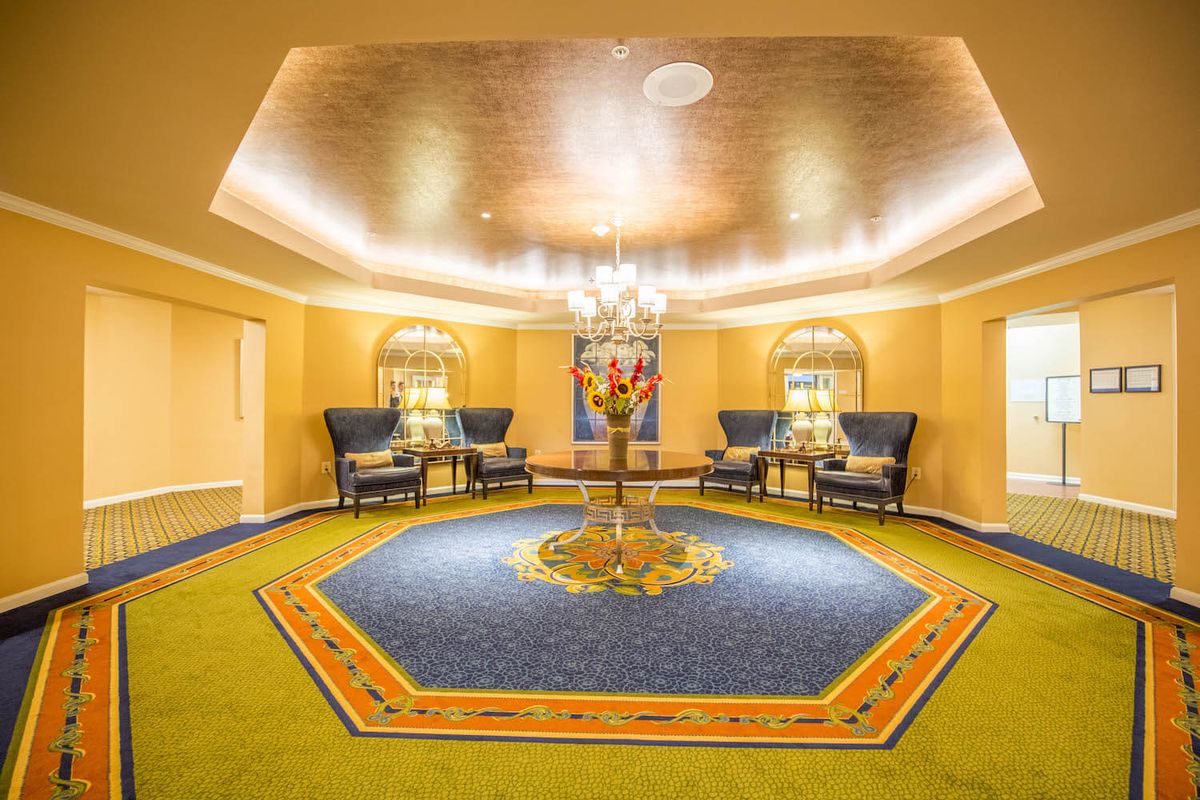 A luxurious lobby featuring a grand chandelier, elegant seating area, and a central table adorned with flowers.