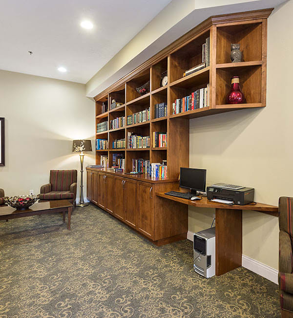 A well-organized office space featuring a large wooden bookshelf, computer setup, and comfortable seating area.