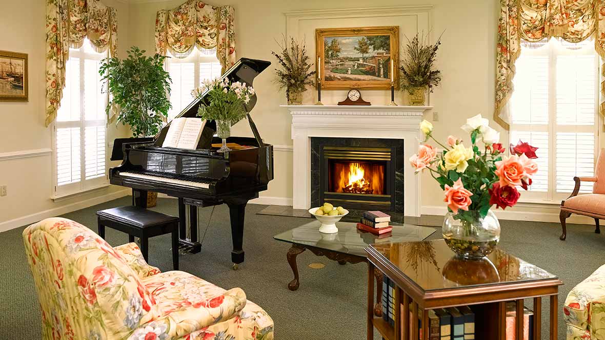 A cozy living room featuring a grand piano and a warmly lit fireplace.