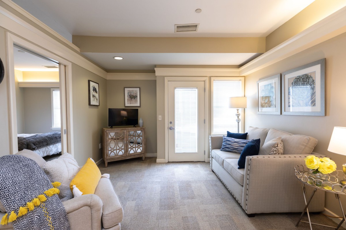 A cozy living room featuring a comfortable couch, decorative pillows, a television set on a cabinet, and soft lighting from a standing lamp.