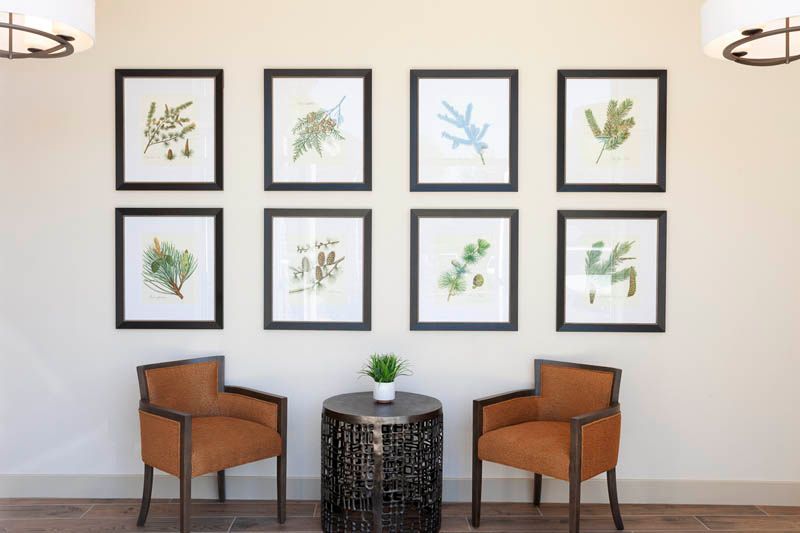 A cozy seating area featuring framed botanical prints, two orange chairs, and a small round table.