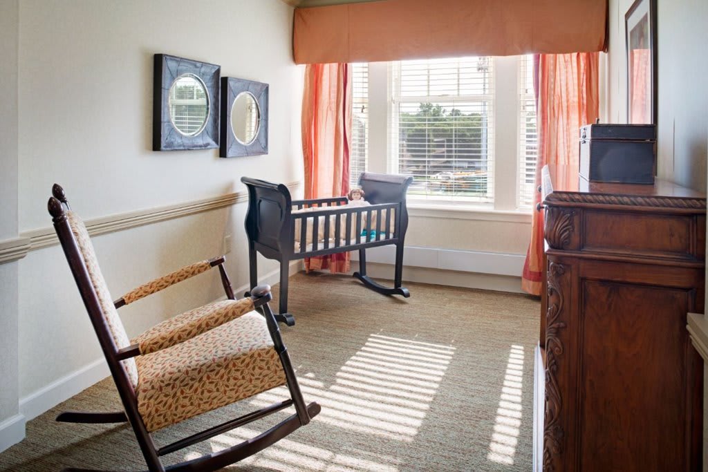 A cozy nursery with a crib and rocking chair by a sunlit window.