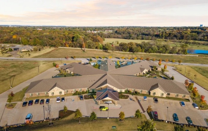 Aerial view of a large building complex with surrounding greenery and parking areas.