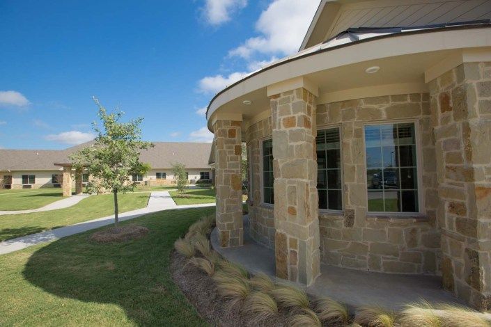 A stone building surrounded by a landscaped lawn and pathways under a clear blue sky.