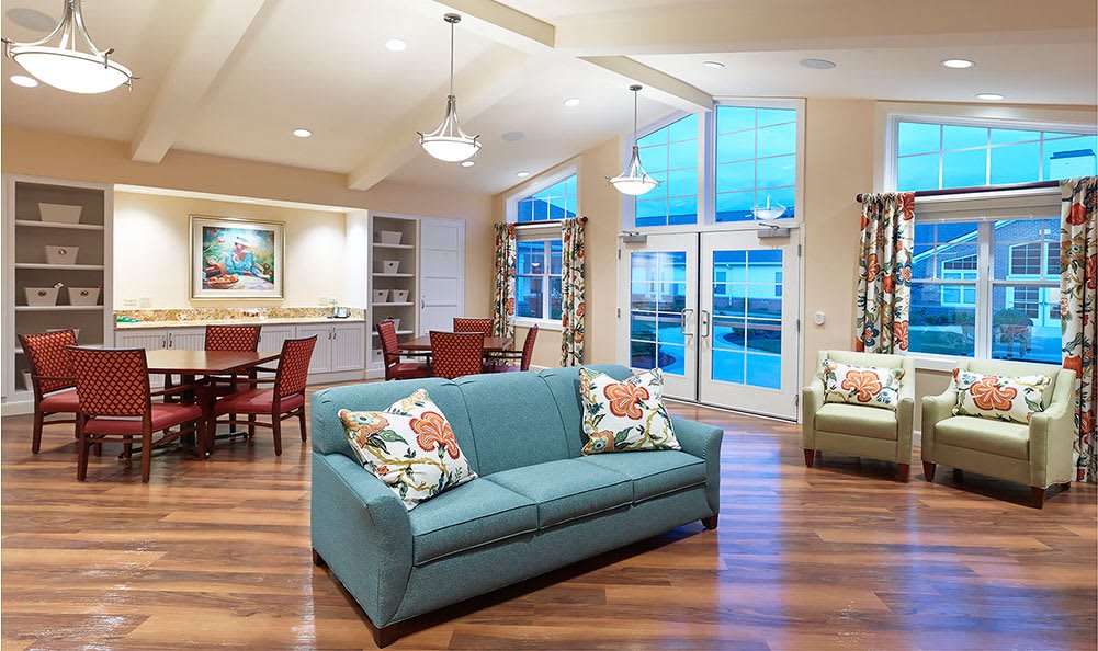 A modern and cozy living room with a blue sofa, wood flooring, and a connected dining area.