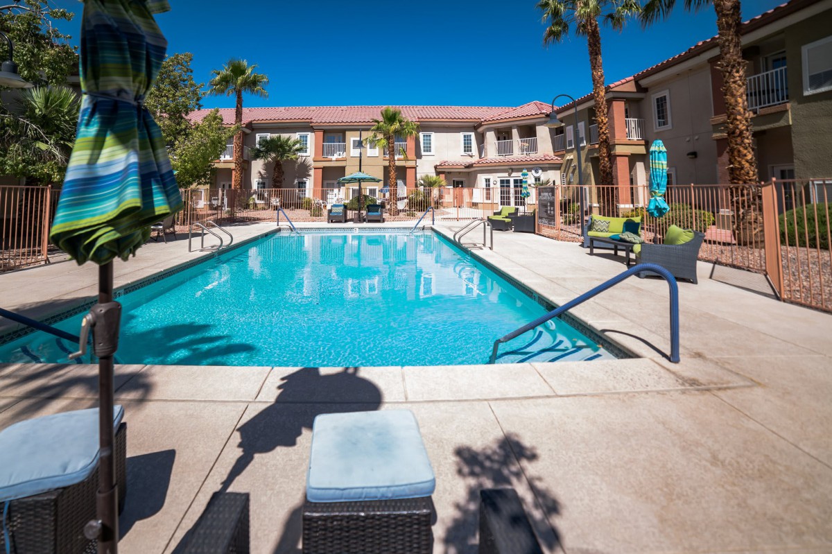 A sunny day at a resort featuring a large outdoor swimming pool surrounded by palm trees.