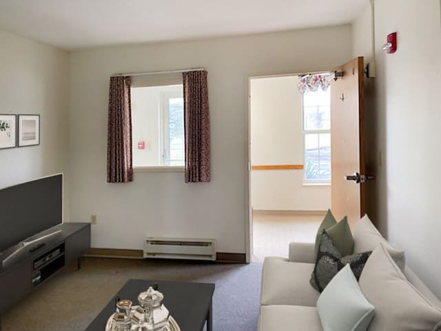 A cozy living room with a sofa, coffee table, and window with curtains.