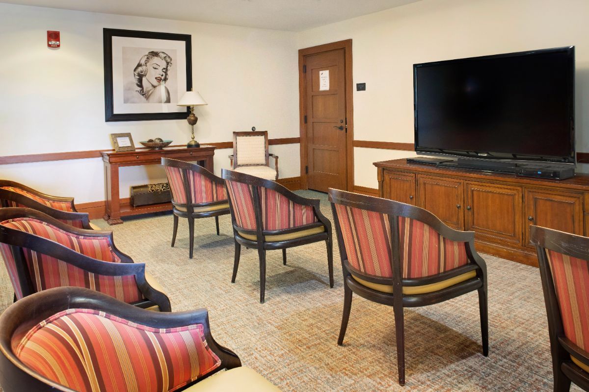 A well-furnished waiting room with chairs facing a television and a painting on the wall.