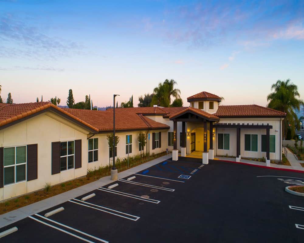 A modern building with a parking lot in front, set against a sunset sky.