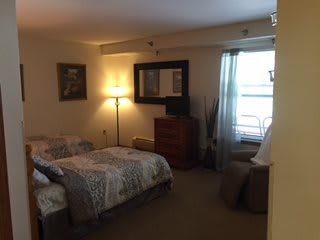 A cozy bedroom with a bed, dresser, mirror, and a lamp near the window.