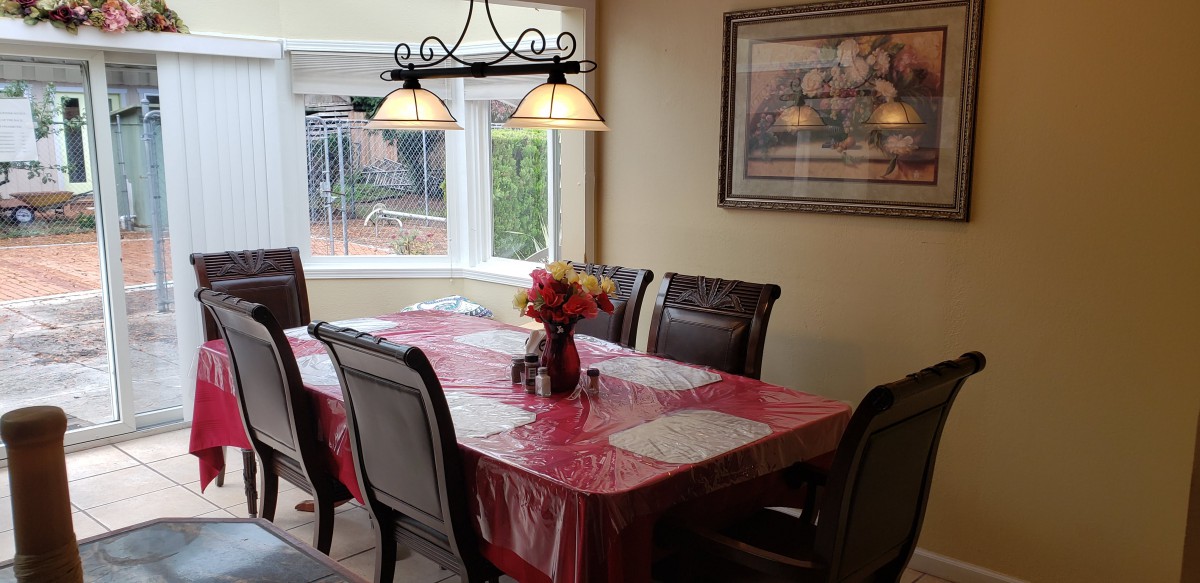 A cozy dining room with a table set for a meal, featuring a red tablecloth and a vase of flowers.