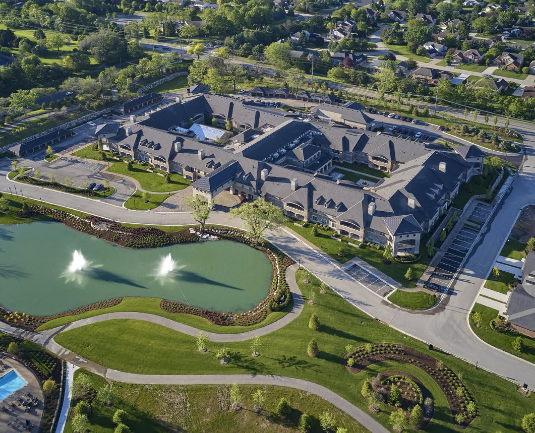Aerial view of a large architectural building surrounded by greenery and a pond with fountains.