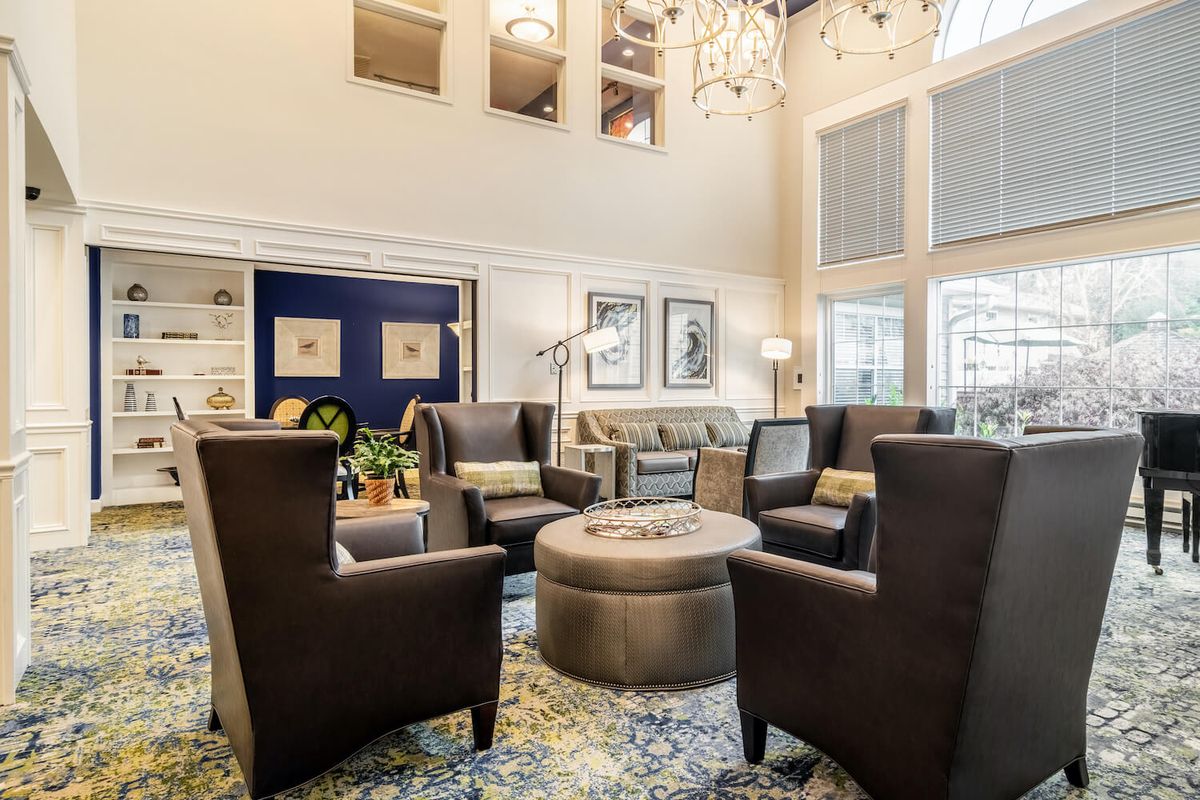 A spacious living room featuring modern armchairs and a chandelier under a high ceiling.