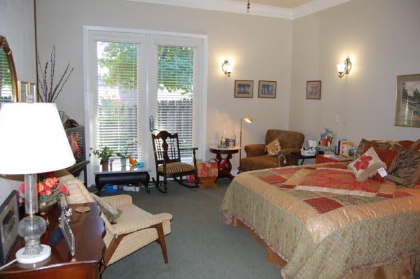 A cozy bedroom with warm decor and comfortable furniture, featuring a bed, armchair, and a window with blinds.