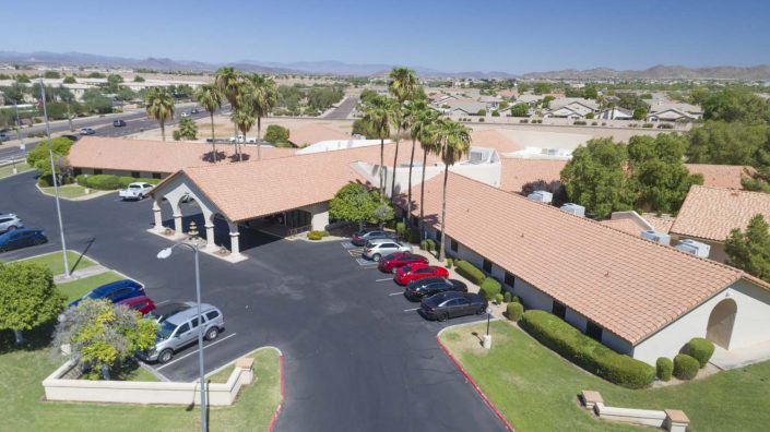 An aerial view of a building with a parking lot and palm trees in a suburban area.