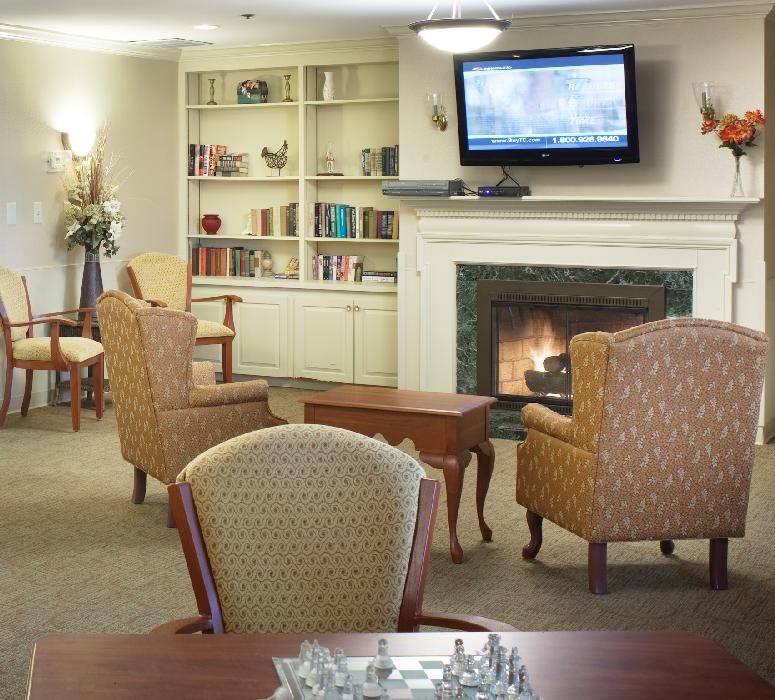 A cozy living room with armchairs facing a fireplace and television, surrounded by bookshelves.