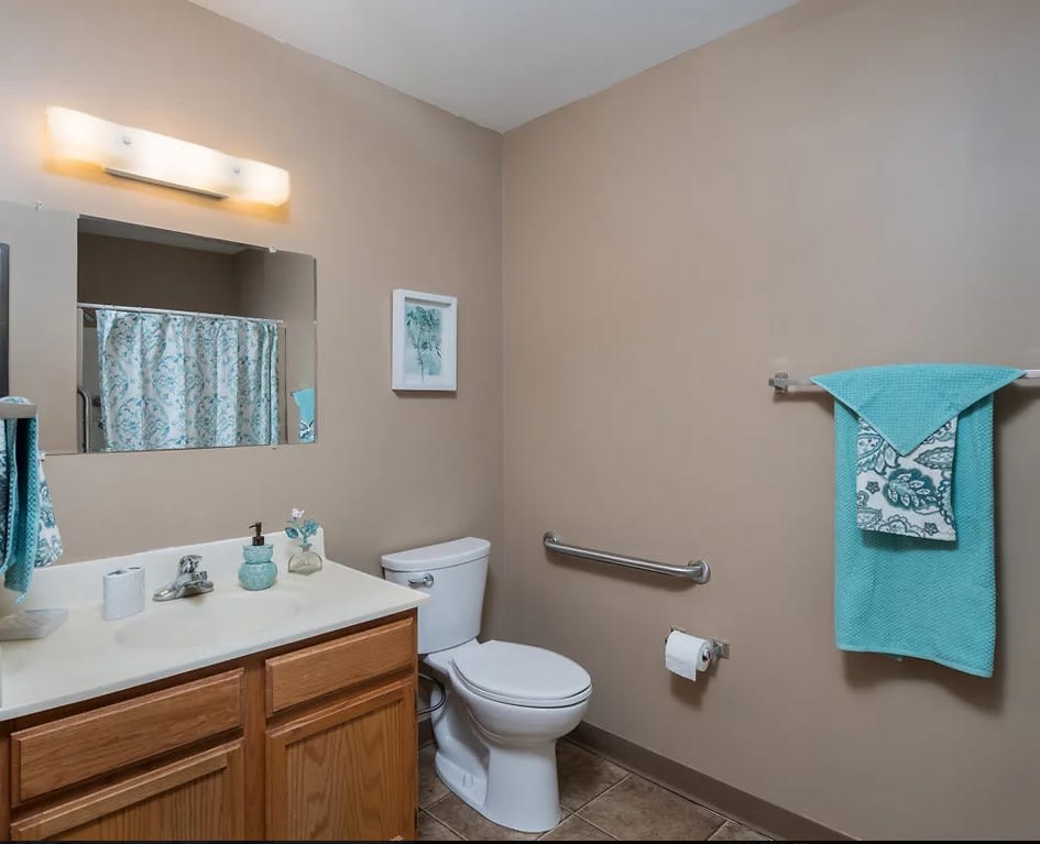 A well-organized bathroom featuring a sink, mirror, toilet, and teal towel accents.