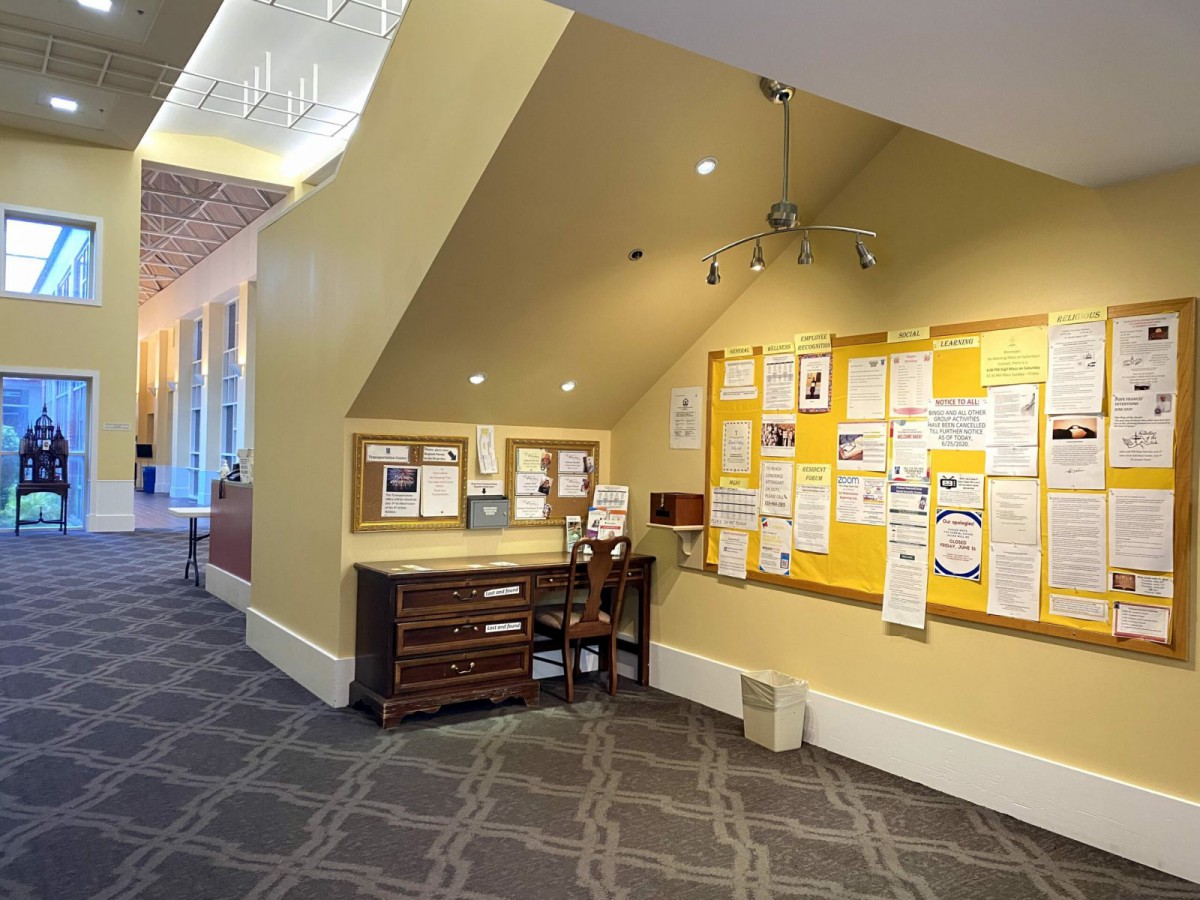 A hallway with a bulletin board and a small desk underneath, featuring various notices and papers pinned up.
