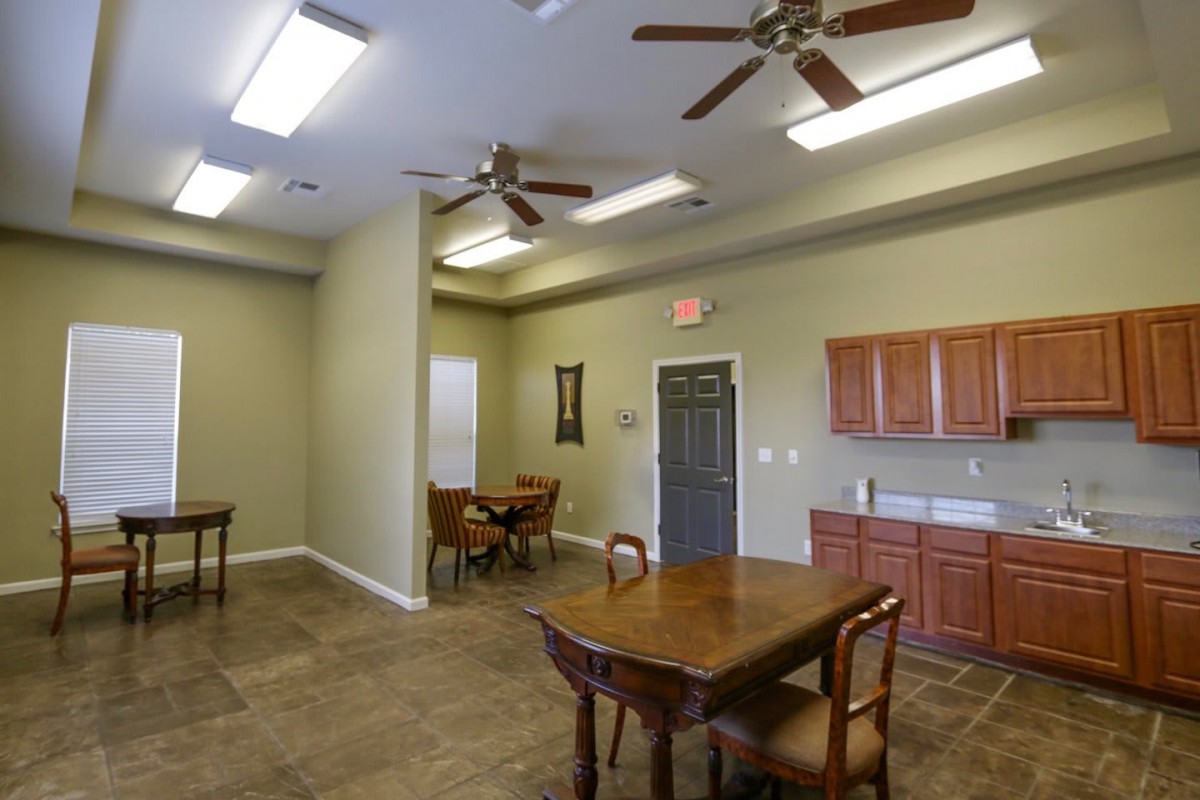 A room with tables and chairs, ceiling fans, and a kitchenette area.