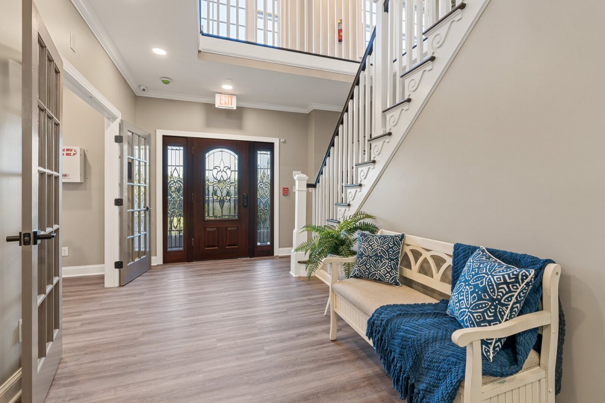 A welcoming foyer with a staircase, wooden flooring, and a decorative bench under natural lighting.