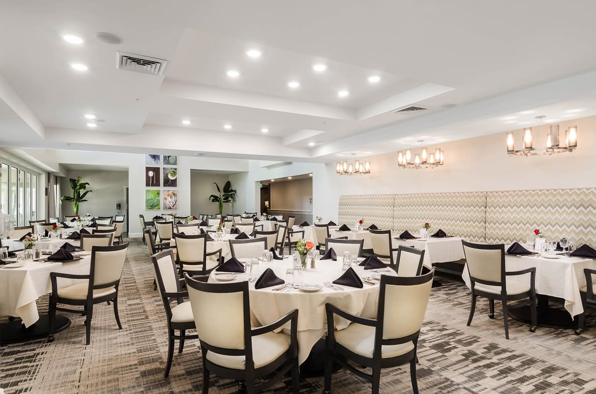 An elegant dining area set for guests, featuring neatly arranged tables and chairs under soft lighting.