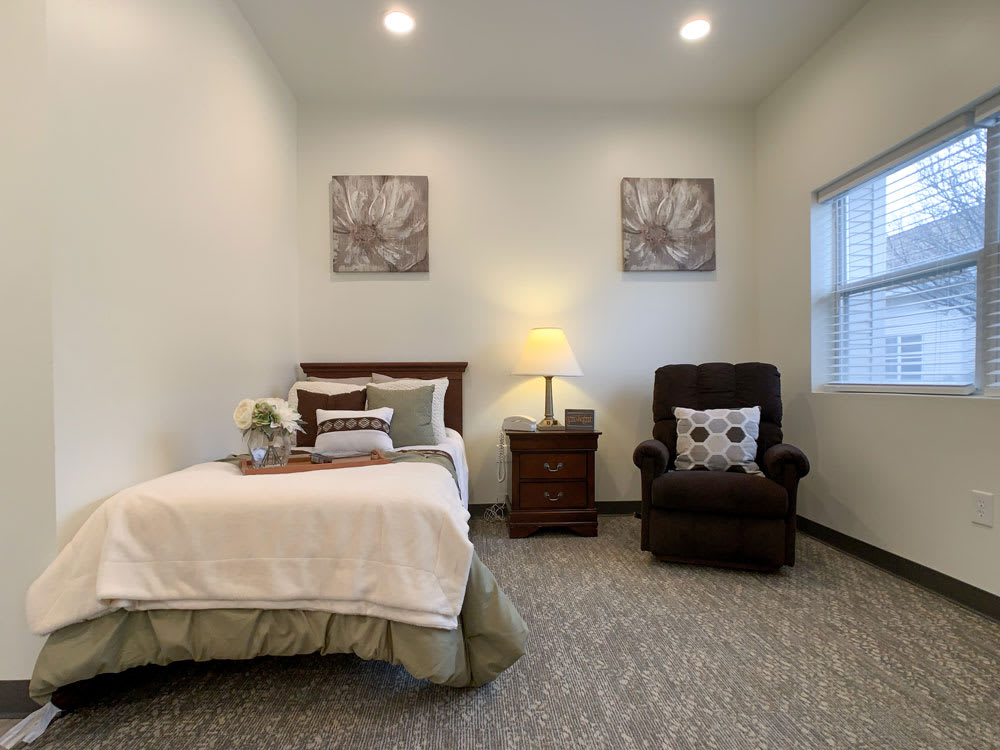 A cozy bedroom with a single bed, bedside table, lamp, and an armchair.