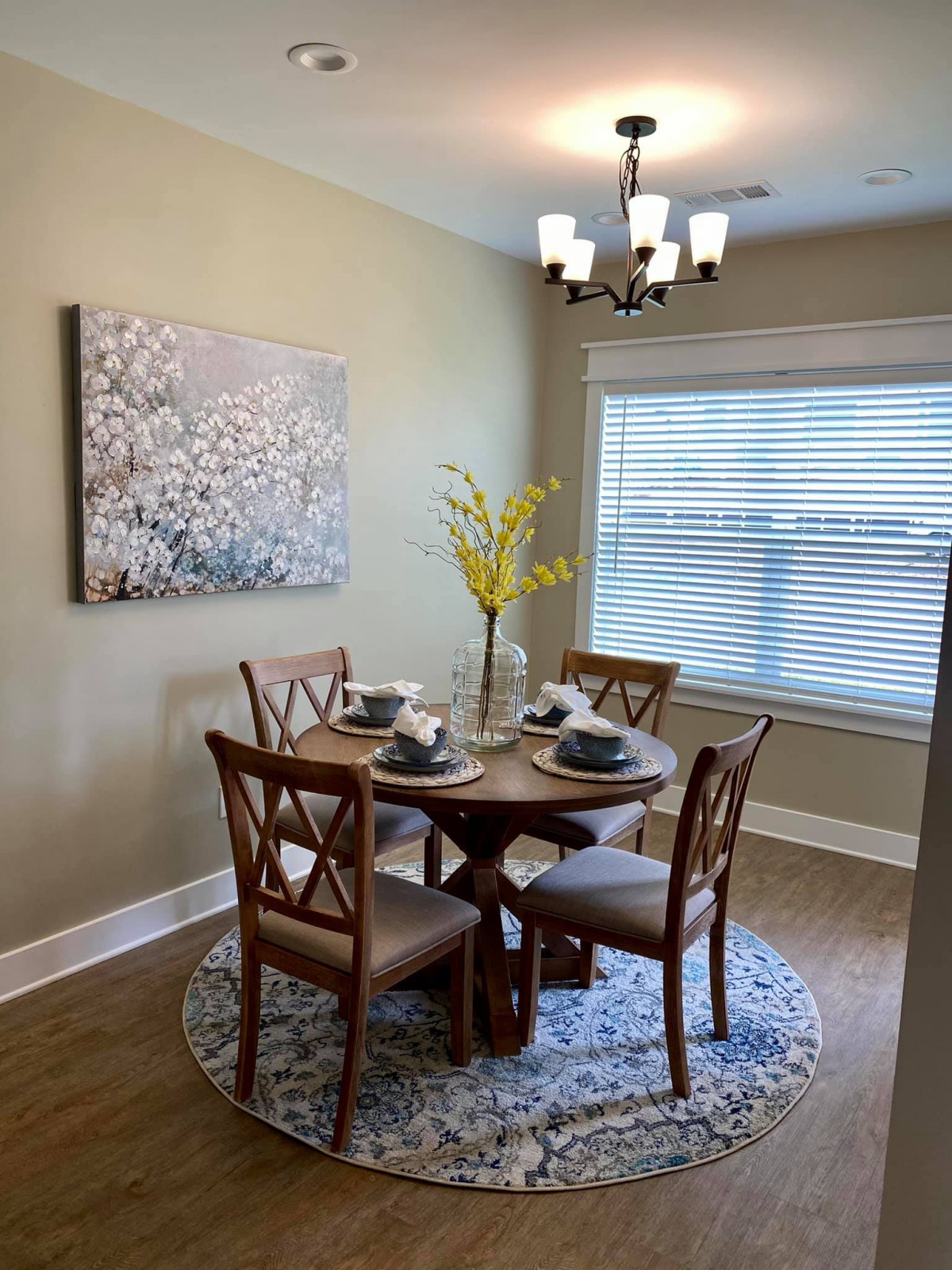 A cozy dining room with a round wooden table set for four, adorned by modern decor and wall art.