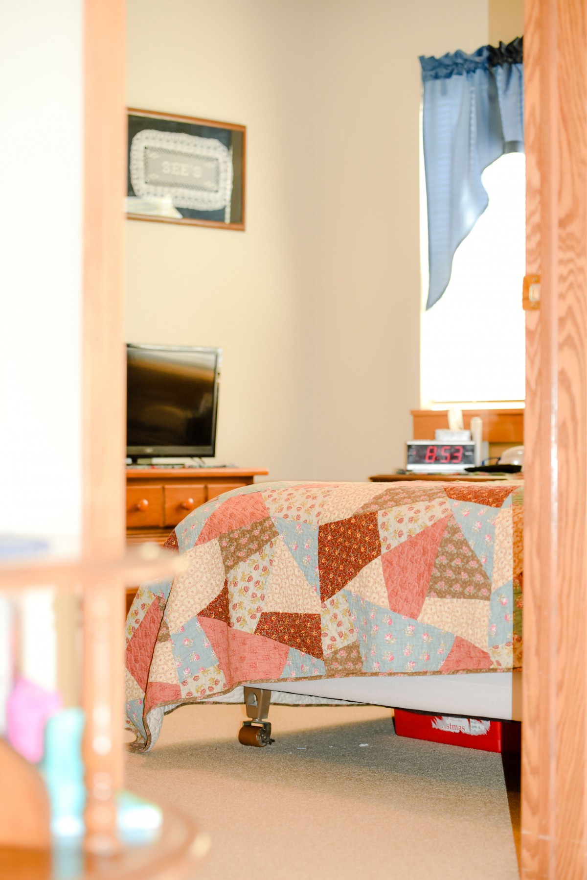 A cozy bedroom with a colorful quilt and a television on a wooden dresser.