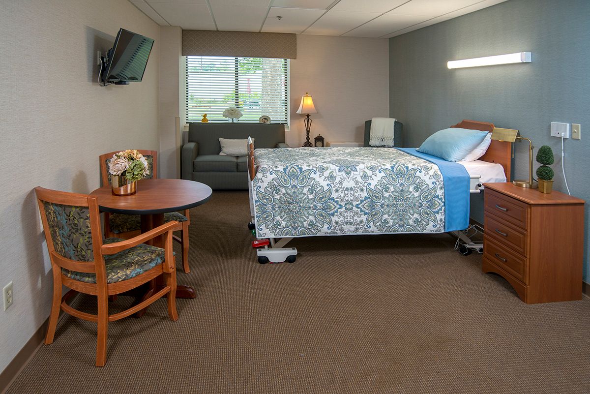 A clean and well-furnished hospital room with a bed, armchair, table, and television.