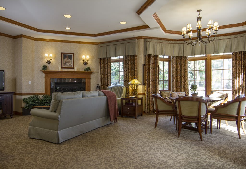 A cozy living room and dining area with traditional decor, featuring a fireplace, comfortable sofa, and elegant chandelier.