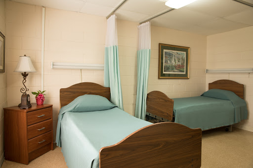 A view of a shared patient room in a hospital, featuring two beds with green bedspreads and curtains for privacy.