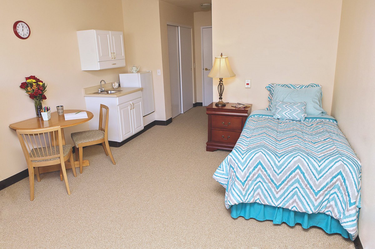 A cozy studio apartment featuring a bed, kitchenette, and dining area.