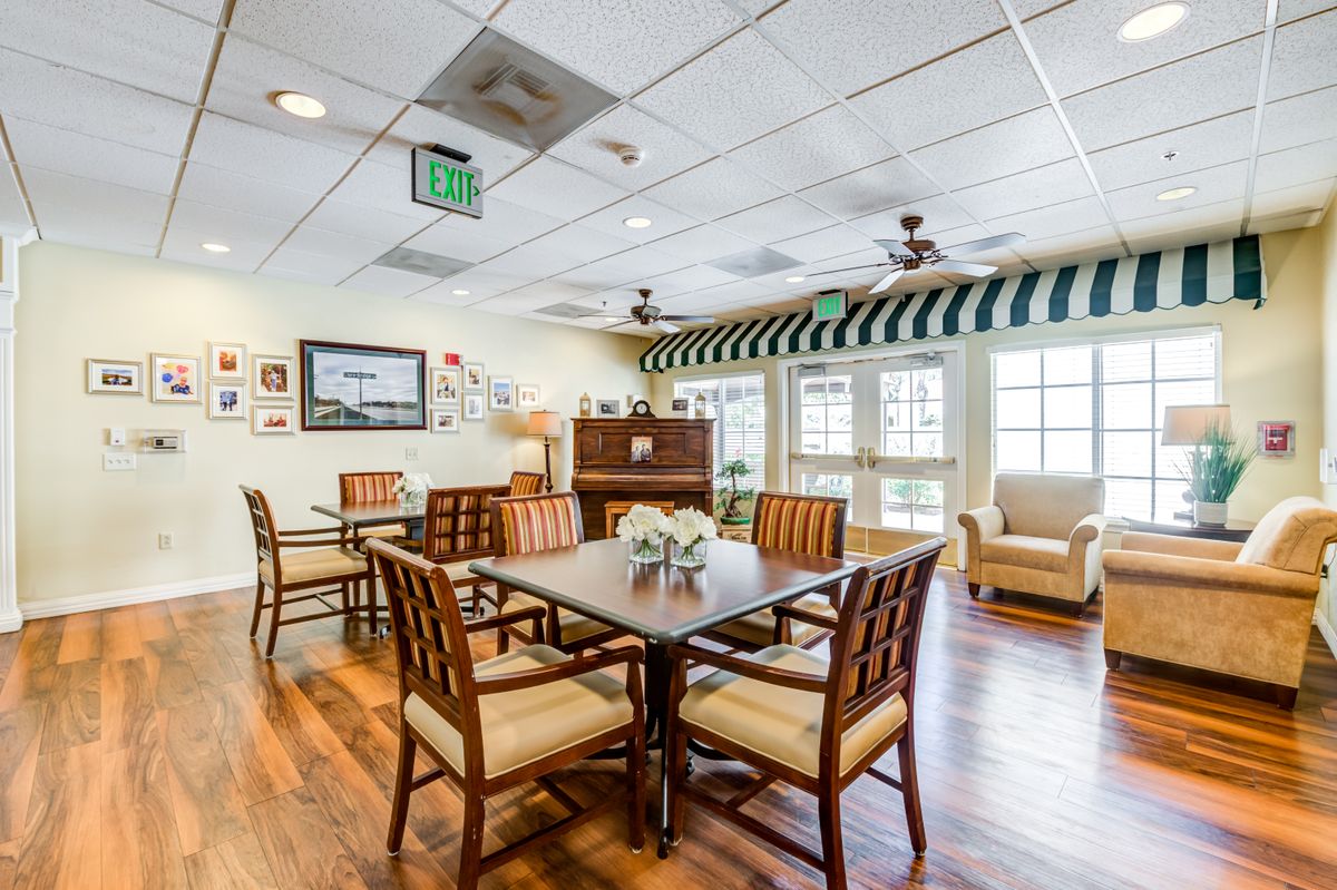A cozy dining area with wooden tables and chairs, framed by large windows and soft lighting.