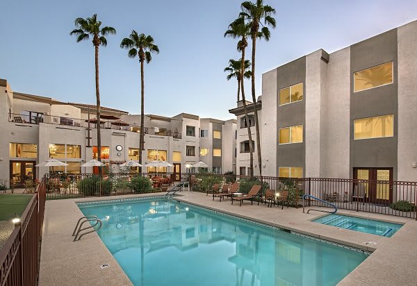A modern apartment complex with a swimming pool and palm trees in the evening.