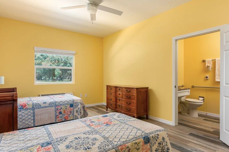 A cozy bedroom with yellow walls, featuring two beds, a wooden dresser, and a ceiling fan.