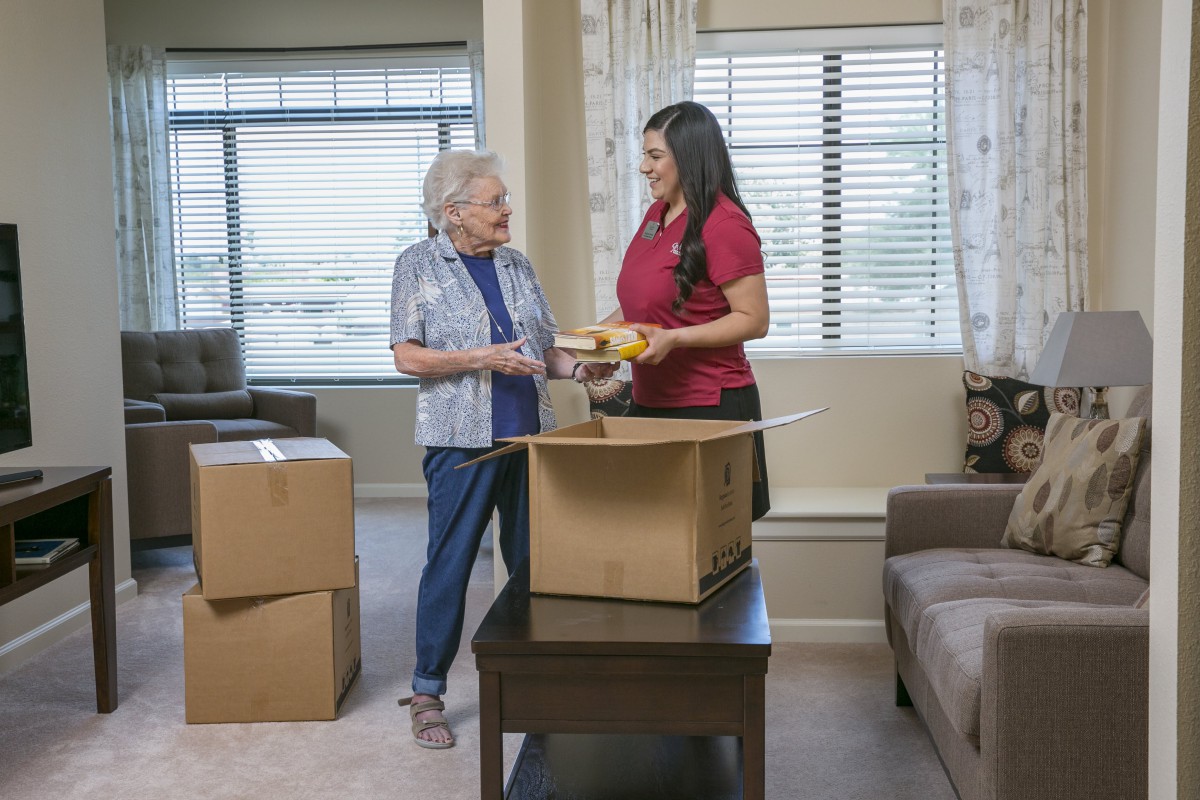 A young woman helps an elderly woman unpack boxes in the living room.