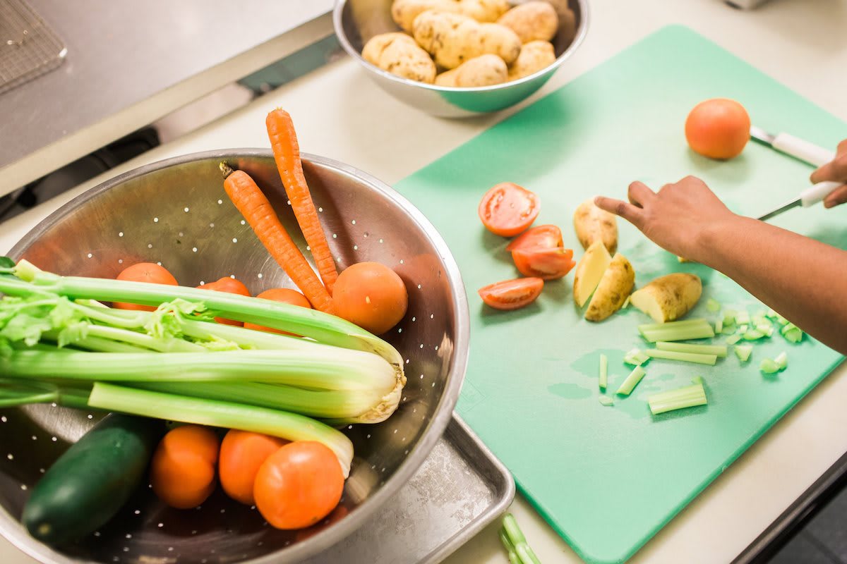 A person preparing vegetables on a cutting board in the kitchen.