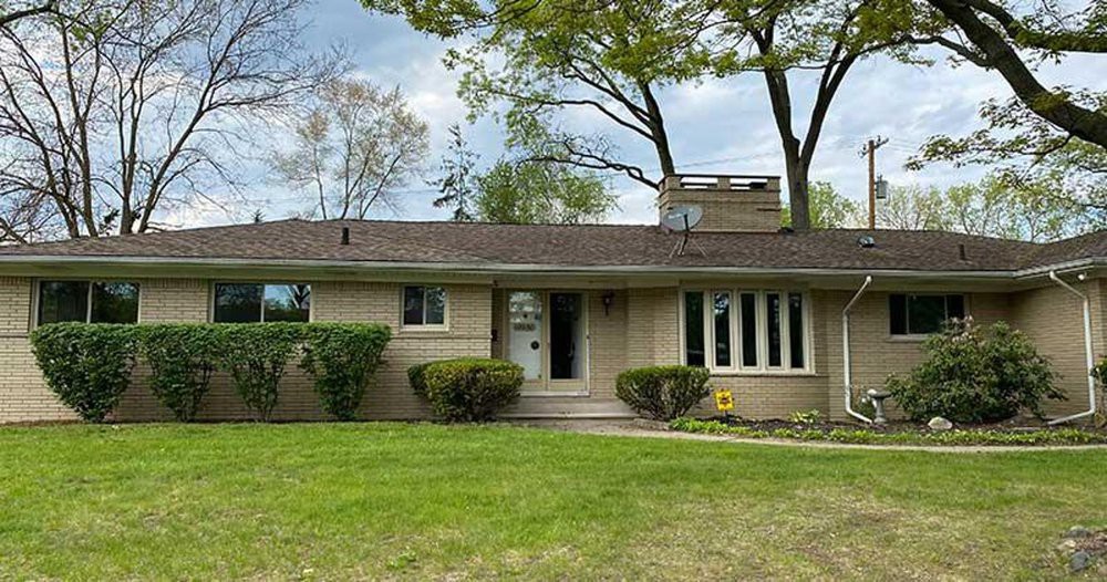 A suburban ranch-style single-story house with a well-maintained lawn and surrounding trees.