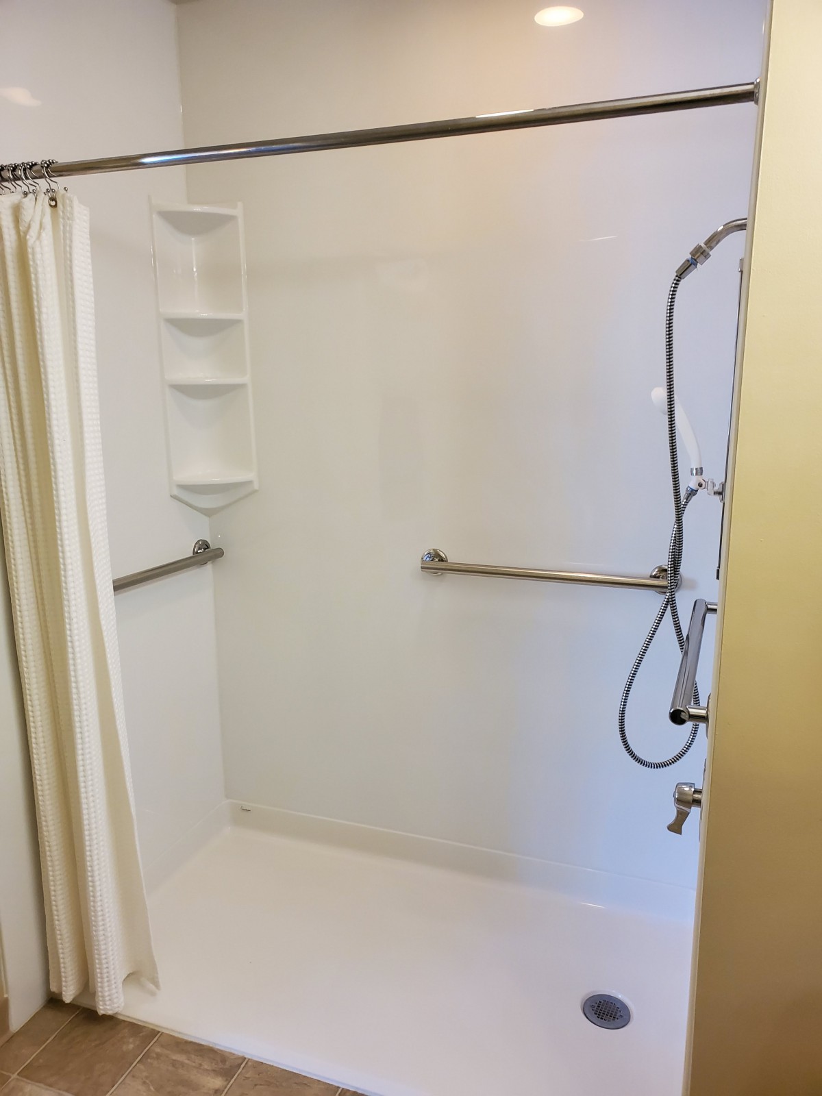 An accessible bathroom shower with grab bars and a wall-mounted showerhead.